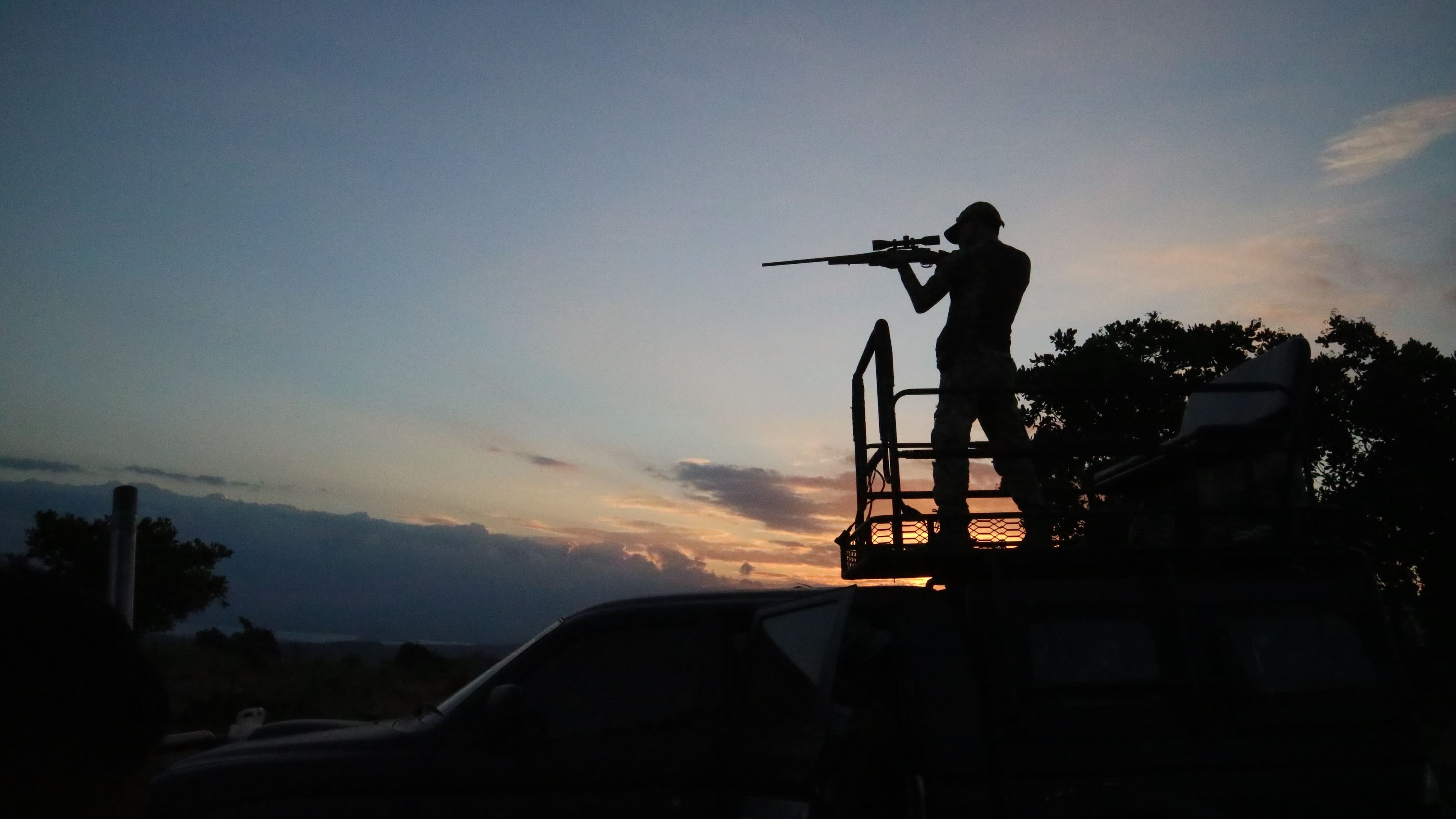 Silhueta de um caçador ao entardecer, sobre a plataforma de um veículo de campo
