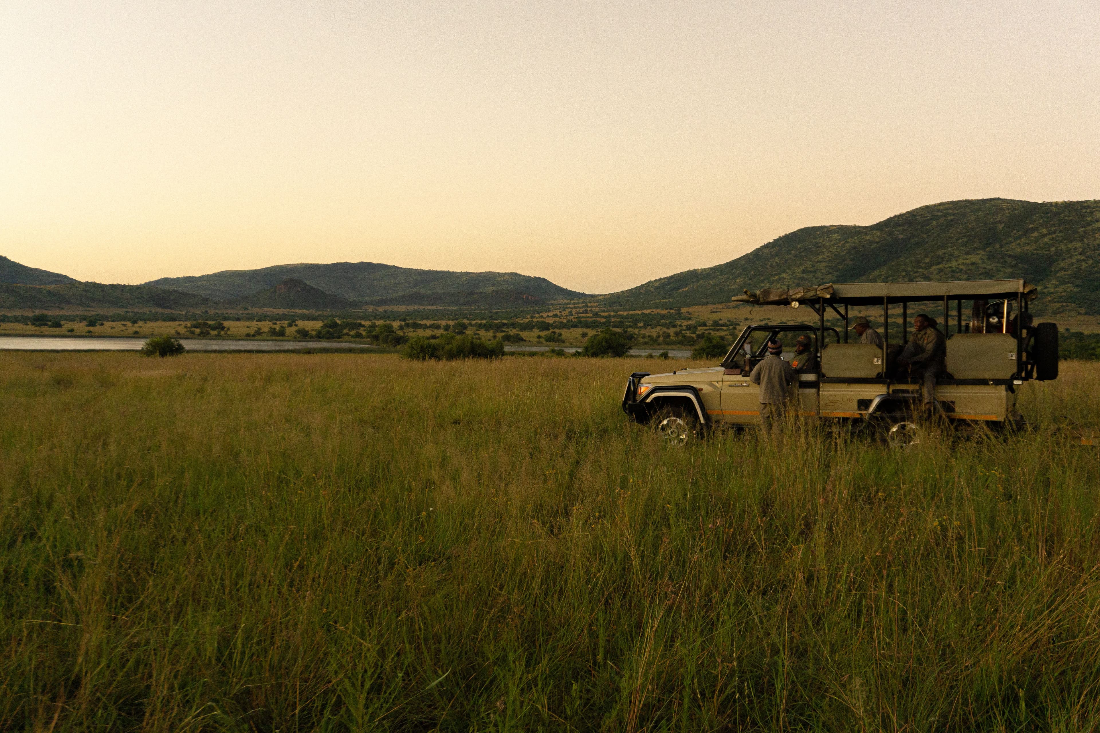 Grupo em veículo de safari parado na pradaria ao entardecer, junto a uma lagoa